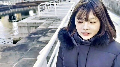 Stunning Asian woman in winter coat on urban dock, thoughtful gaze