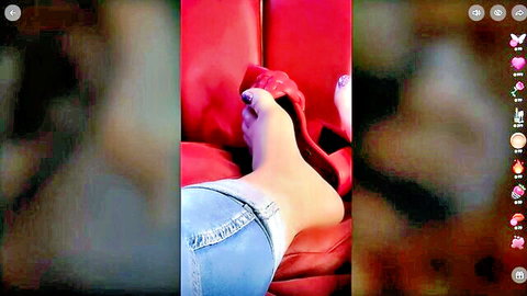Woman lounging with bare feet slipped from red high heels, denim shorts