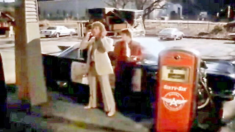 Vintage retro brunette in white suit smoking cigarette next to man at gas station