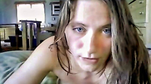 Topless blue-eyed webcam girl stares intensely at camera exposing bare tits in bedroom