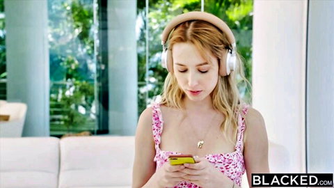 Blonde babe in skimpy pink top wearing headphones checks phone in luxury room