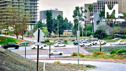 Busy Los Angeles intersection with cars circling roundabout amid skyscrapers and palm trees