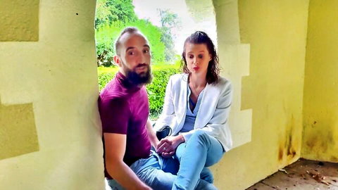 Smiling brunette woman in blazer holds hands with bearded man in purple shirt outdoors