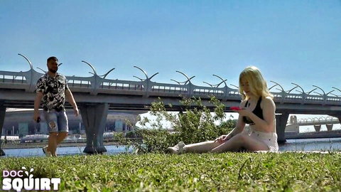 Blonde Luna Umberley in pink bikini sitting outdoors by river bridge