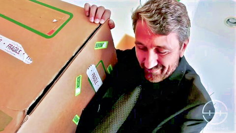 Older man smiling while carrying fragile box with petite Asian sex doll inside