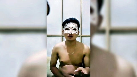 Topless Asian man in white skull mask, sitting intimately