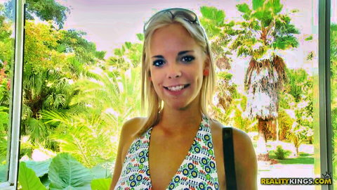 Blonde babe smiling with deep cleavage in colorful low-cut top by tropical window