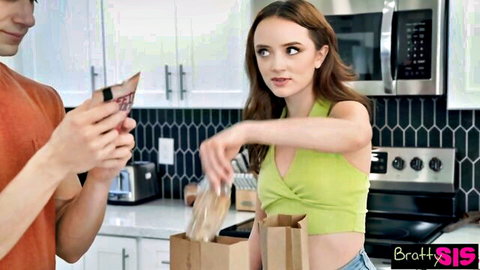 Bratty stepsister in tight green top and shorts pours snacks into bowl in kitchen with stepbro