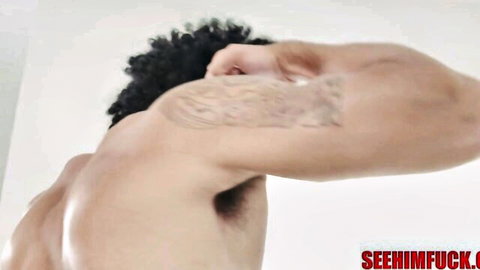 Muscular black stud with tattoo flexes arm shirtless from behind