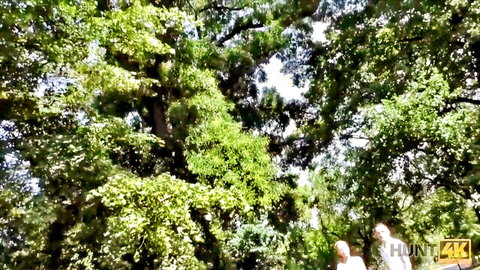 Mature woman in white dress walks with older man in sunny forest for cash sex encounter