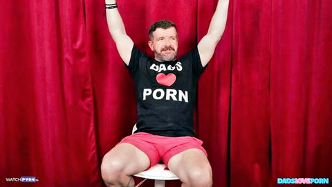Muscular DILF in Dads Porn shirt flexing arms up wearing tight pink shorts on red curtain stage