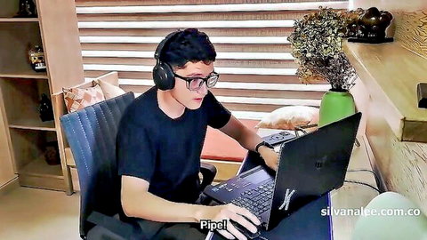 Young man with glasses and headphones typing on laptop at wooden desk