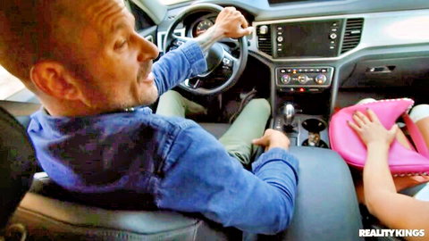 Mona Azar in car seat holding pink hat, driver beside her, Reality Kings