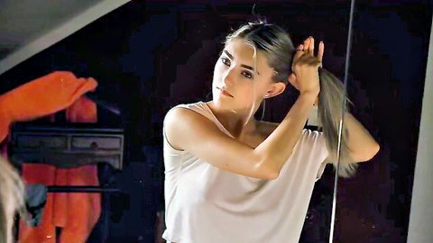 Eva Elfie tying silver ponytail in white tank top, mirror pose