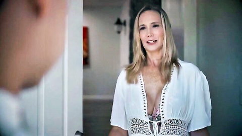 Lilly James as blonde stepmom in low-cut white dress showing cleavage