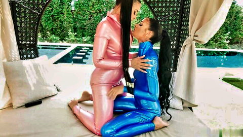 Two ebony women in shiny pink and blue catsuits kissing passionately poolside