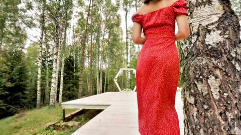 Petite brunette in tight red polka dot off-shoulder dress poses back view by birch tree in forest wedding arch