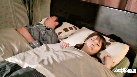 Japanese brunette smiling blissfully in bed beside sleeping man