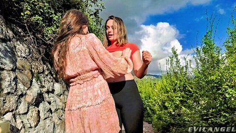 Two sexy brunettes in crop tops and tight pants flirt outdoors by stone wall