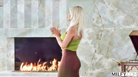 Blonde MILF with big ass and huge tits teases in tight skirt by fireplace