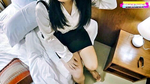 Thai woman in white blouse and black skirt sitting on bed, teasing legs