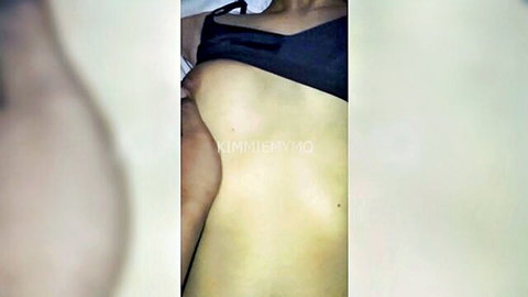 Petite Thai teen with small tits exposed from black bra lying topless on bed