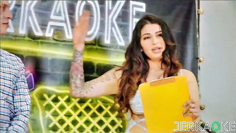 Sexy tattooed brunette babe in skimpy white top holds clipboard at Jerk Off Karaoke