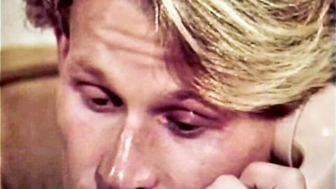Blonde man with intense eyes talking on vintage rotary phone closeup