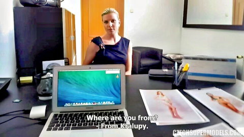 Blonde model in tight blue dress smiles seductively at desk during casting audition