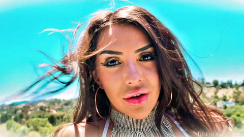 Brunette beauty with glossy plump lips and wind-swept long hair posing seductively outdoors
