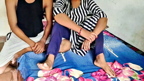 Indian couple holding hands intimately on bed, her striped dress hiked up showing bare feet and leggings