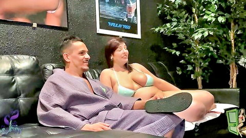 Curvy brunette in green bikini teases man in robe on couch