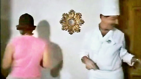 Vintage 1982 couple scene, woman in pink top from behind with chef man