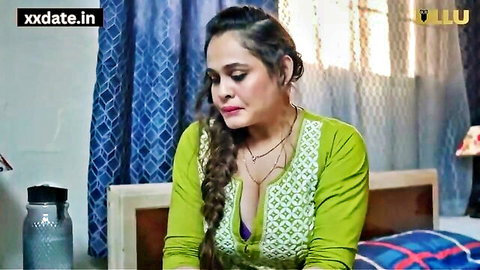 Busty Indian MILF housewife in low-cut green blouse showing deep cleavage on bed