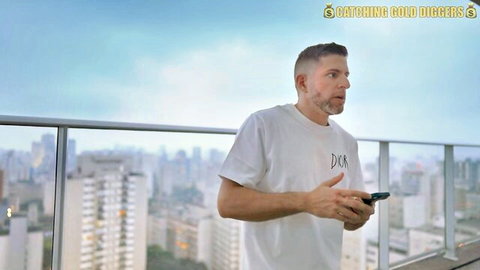 Handsome man in white Dior shirt holding phone on balcony overlooking city skyline