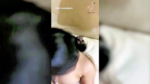 Innocent-faced Asian teen girl lying in bed with dark hair bun