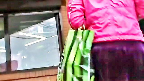 Asian woman in pink tracksuit holding green bag, taut booty view in public setting