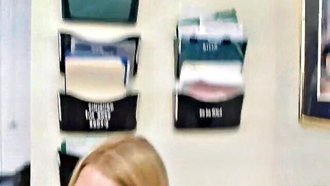 Blonde hair visible behind stacked green and beige office magazine file holders on wall