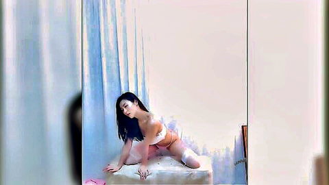 Seductive Asian woman in beige lingerie kneeling and stripping on bed