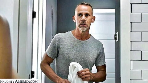 Mature man in gray t-shirt holding white towel in modern tiled bathroom mirror