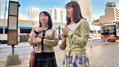 Two slim Asian women in casual cardigans and skirts at urban bus stop