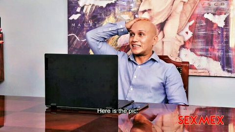Bald smiling man in blue shirt at office desk with laptop and SexiMex watermark