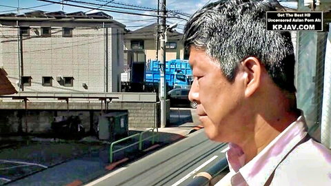 Mature Japanese man in pink shirt on balcony overlooking urban street