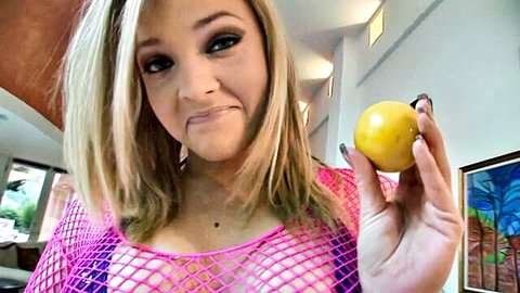 Blonde babe in sheer pink fishnet top teases with lemon at pouty lips, perky tits visible