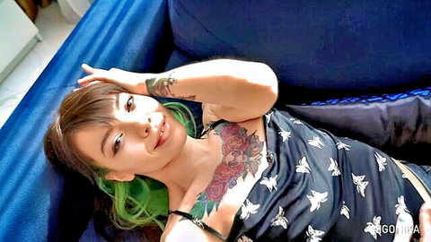Tattooed green-haired babe lounging on couch teasing deep cleavage and rose tattoo on tits