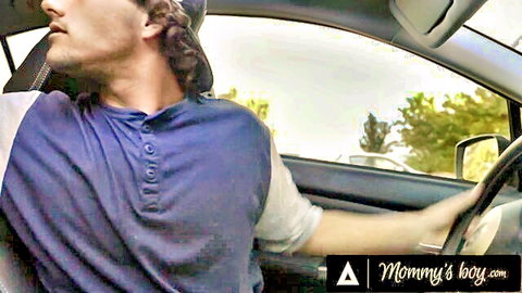 Handsome curly-haired man in purple shirt driving car with cap on Mommy's Boy site