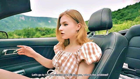 Young blonde teen in checkered top gestures seductively in open convertible car amid forest mountains POV