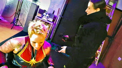 Blonde Captain Marvel cosplayer in doggy style ready for strapon pegging by brunette in fur coat