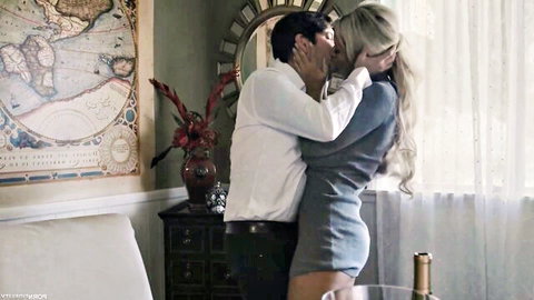 Blonde woman in tight gray dress passionately kissing man's neck in steamy indoor embrace