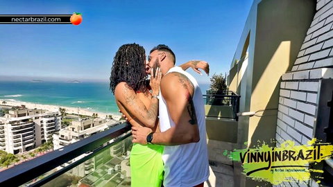 Tattooed Brazilian couple passionately kissing on sunny ocean balcony